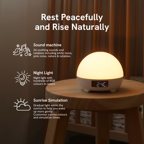 A dome-shaped digital alarm clock lamp glowing with warm light on a wooden table, with promotional text on the left highlighting sound machine, night light, and sunrise simulation features.